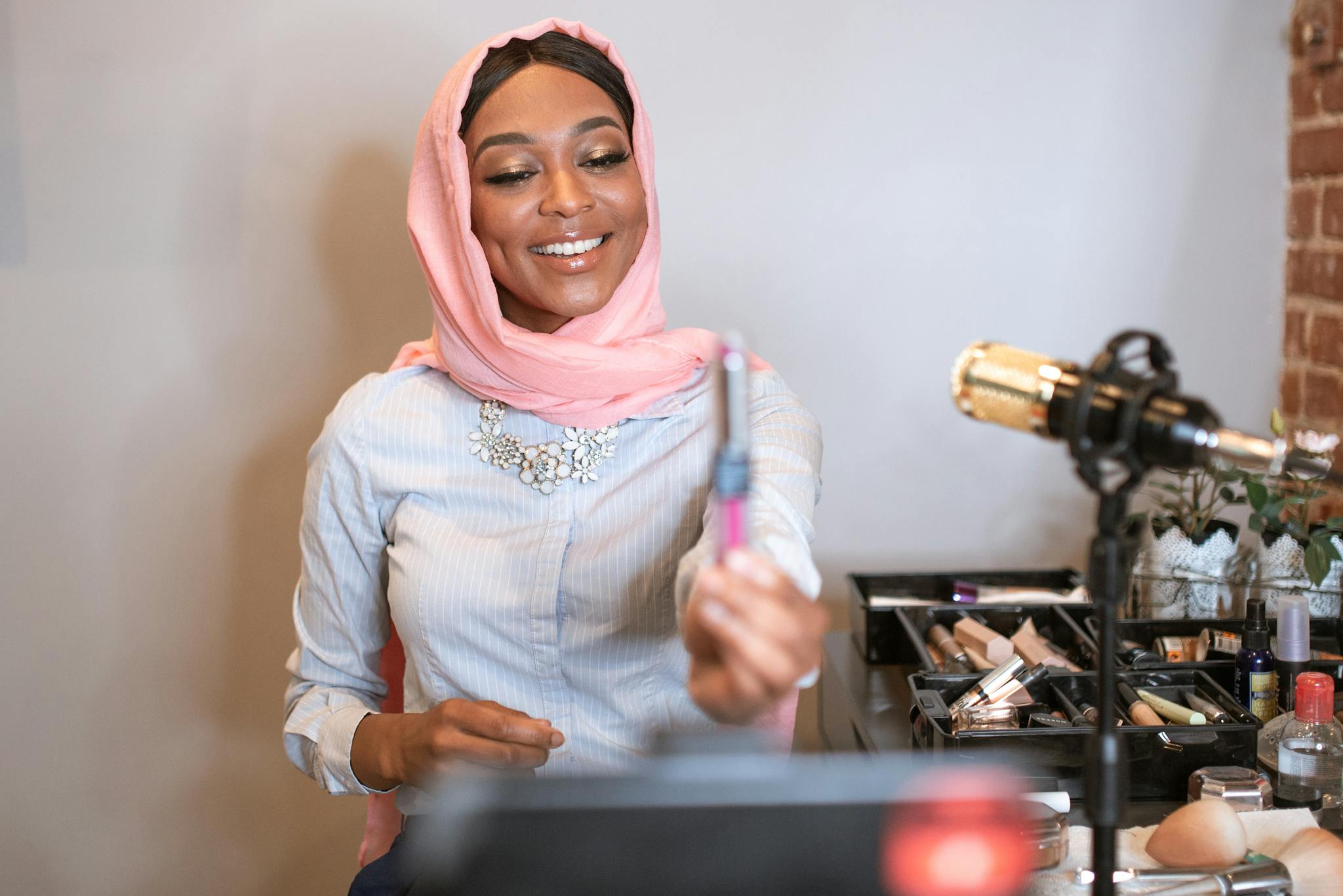 A smiling Muslim woman wearing a hijab records a makeup tutorial for her vlog.